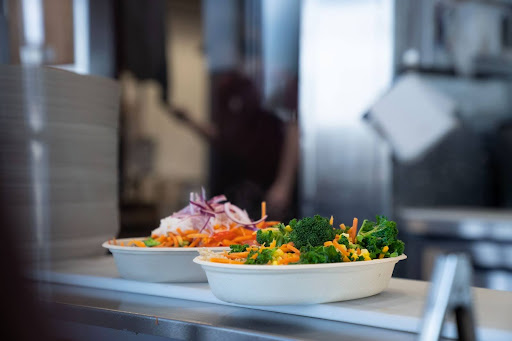 A Balance Grille chef adding sliced red peppers into a nutrient-rich rice bowl with customizable toppings.